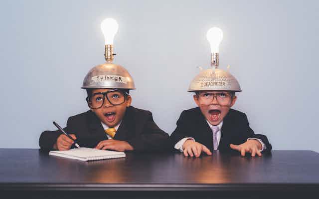 Two children in suits wearing lightbulb-topped metal caps, one of which is inscribed "Thinker" and the other "Ideaometer"