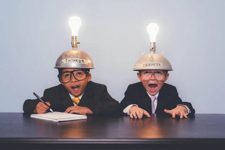Two children in suits wearing lightbulb-topped metal caps, one of which is inscribed "Thinker" and the other "Ideaometer"