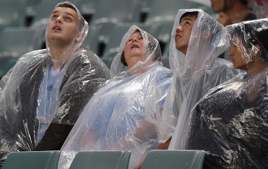 spectators in rain ponchos look at the sky