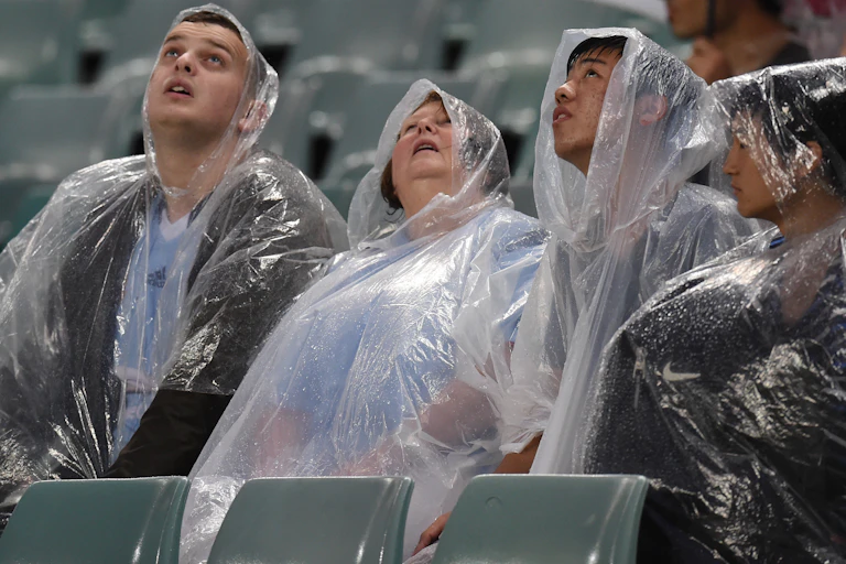 spectators in rain ponchos look at the sky