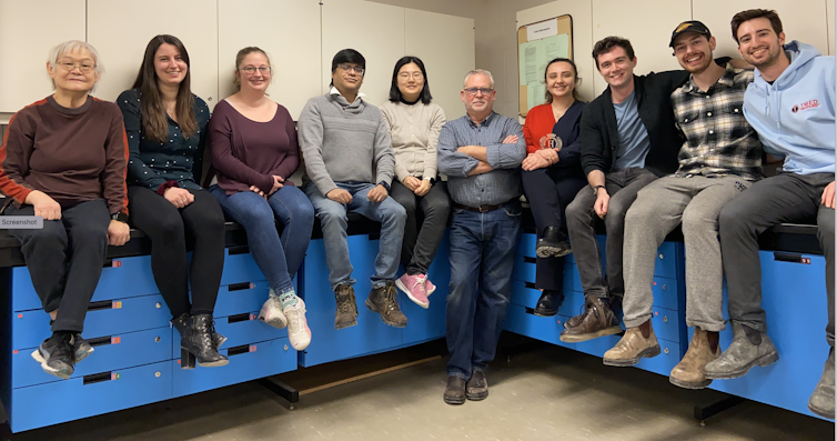 A group of people sitting on blue storage drawer units in a V formation.