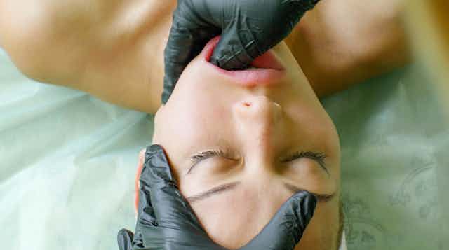 Beauty therapist performing buccal massage on woman