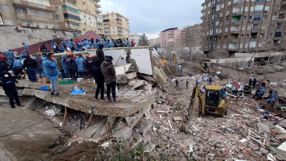 Bystanders watch from a collapsed building as diggers search in the wreckage
