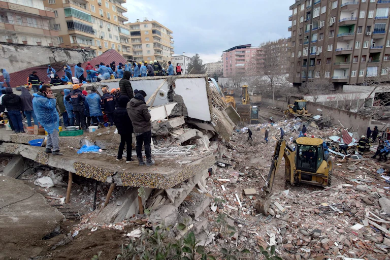 Bystanders watch from a collapsed building as diggers search in the wreckage