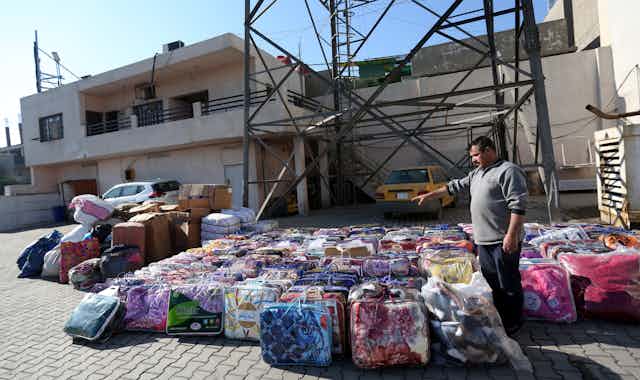 A man gestures at stacks of packages of aid for earthquake victims in Syria.