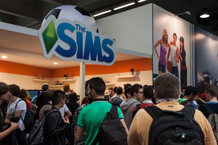 A large sign reads The Sims - fans stand beneath.
