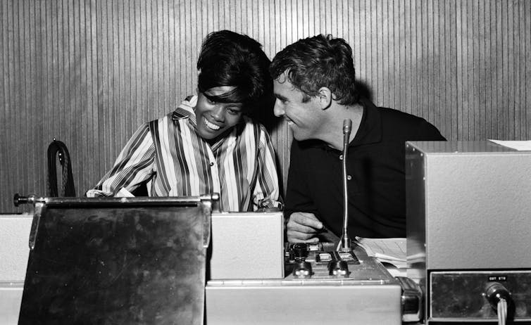 A mana and woman sit at a recording desk.