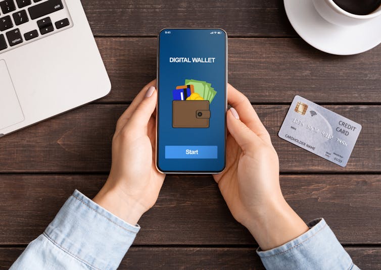 Mobile banking. Woman holding smartphone with digital wallet application. credit card on table, top view