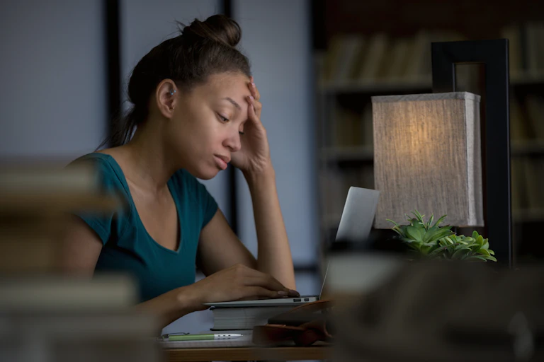 Young woman in blue T-shirt sits in front of laptop and looks tired