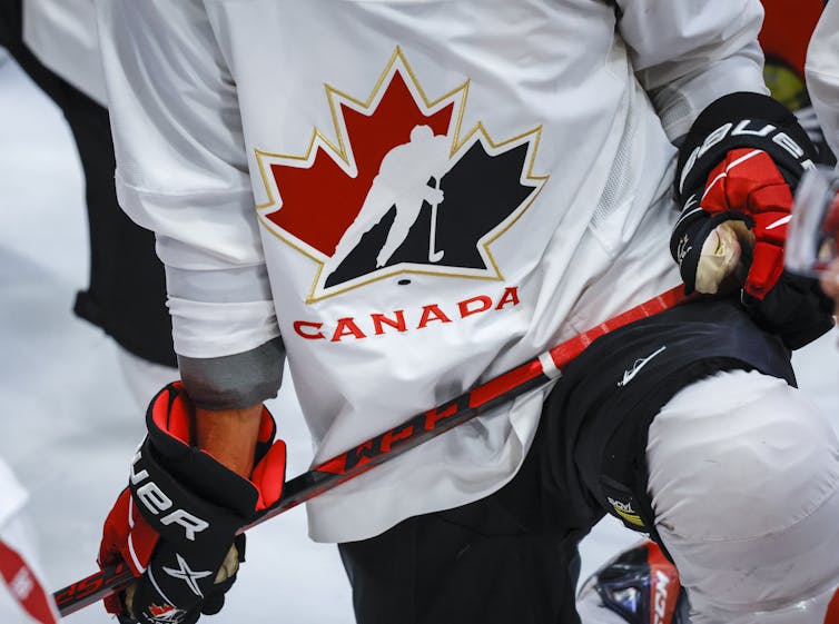 A Hockey Canada logo is shown on the jersey of a player carrying a hockey stick.
