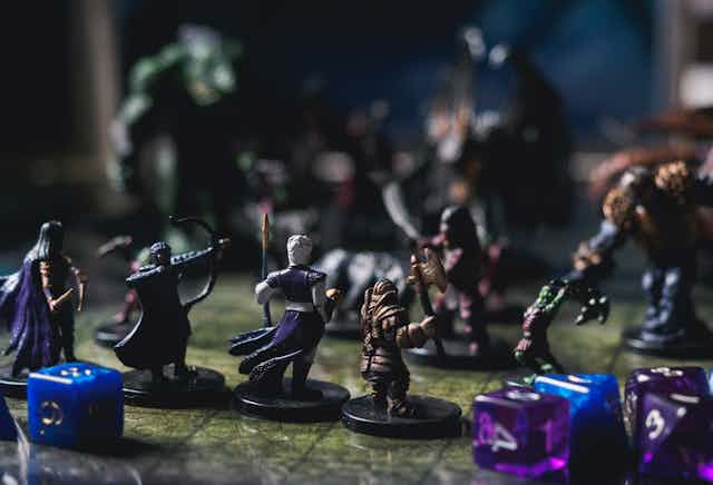 Mini figurines of fantasy characters sit on a tabletop game board. In the background, monster figures sit on the board, facing the fantasy character figurines.