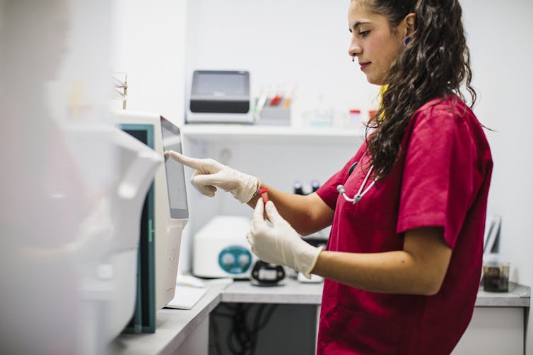 Lab technician holding blood tube and setting up machine for analysis