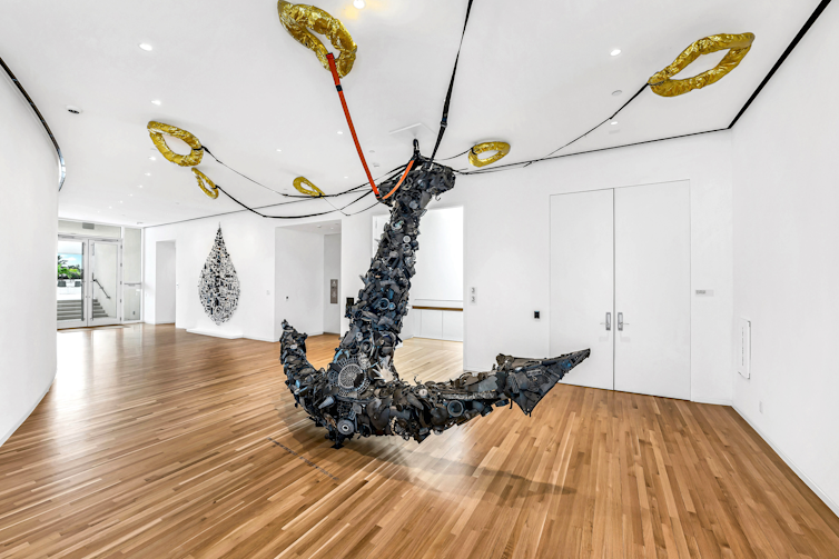 A giant sculpted anchor in an art gallery, with ties to gold life preservers mounted on the ceiling.