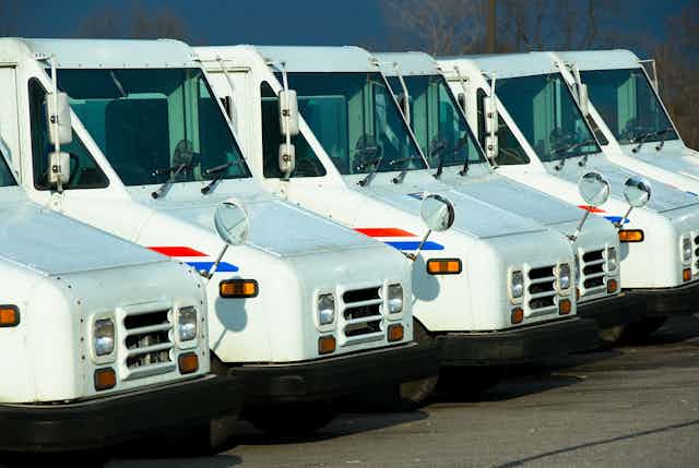 Half a dozen postal service trucks lined up in a row.