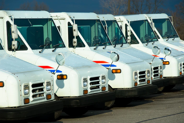 Half a dozen postal service trucks lined up in a row.