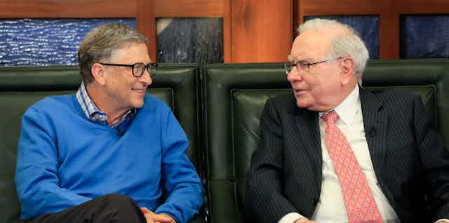 A man in a blue sweater speaks with an older gentleman in a suit and tie