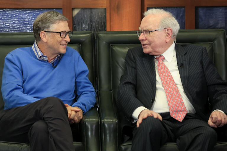 A man in a blue sweater speaks with an older gentleman in a suit and tie