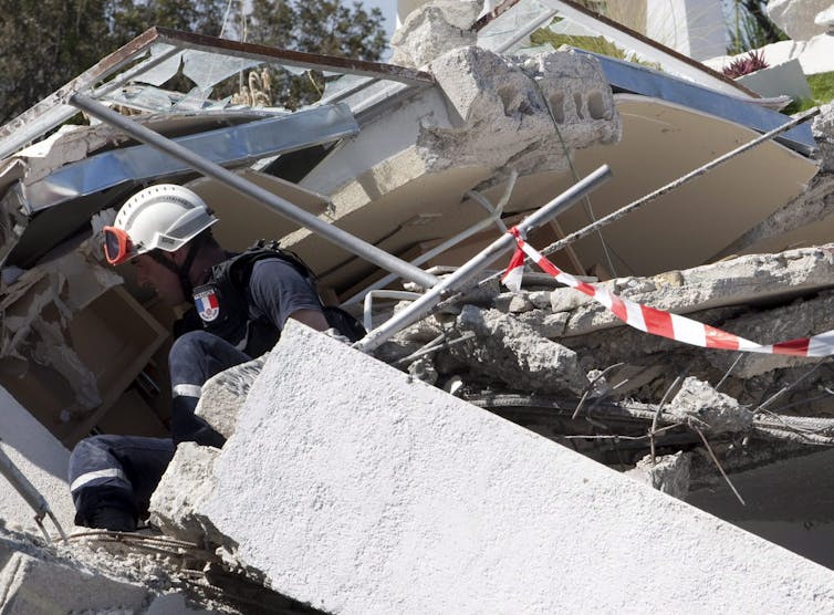 a rescue worker with a white helmet and a French emblem hunches down in debris