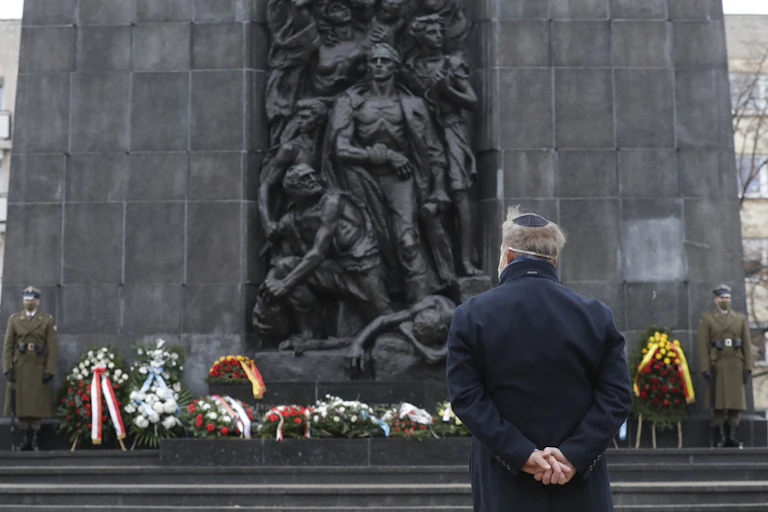 A man stands in front of a large statue of people..