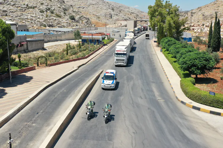 Police vehicles lead a convoy of trucks carrying aid into Syria