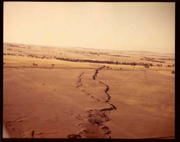 A photo showing a crack running through reddish ground into the distance.