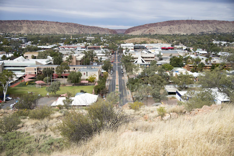 A view of Alice Springs from Anzac Hill. It's a sunny day and there are hills in the distance with dark blue clouds behind them.