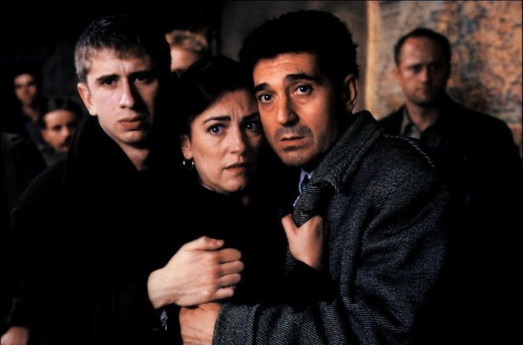 A woman and two men look at the camera in anguish.