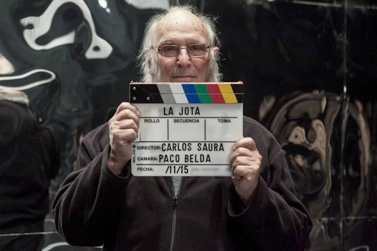 A man looks at the camera holding a clapperboard.