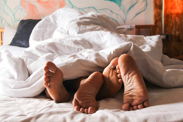 Two pairs of feet poking out under bedsheets.