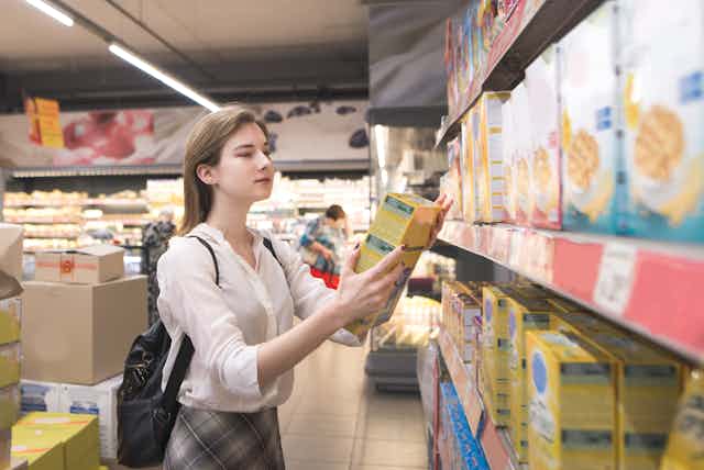 una mujer en un supermercado leyendo los textos de una caja de cereales.