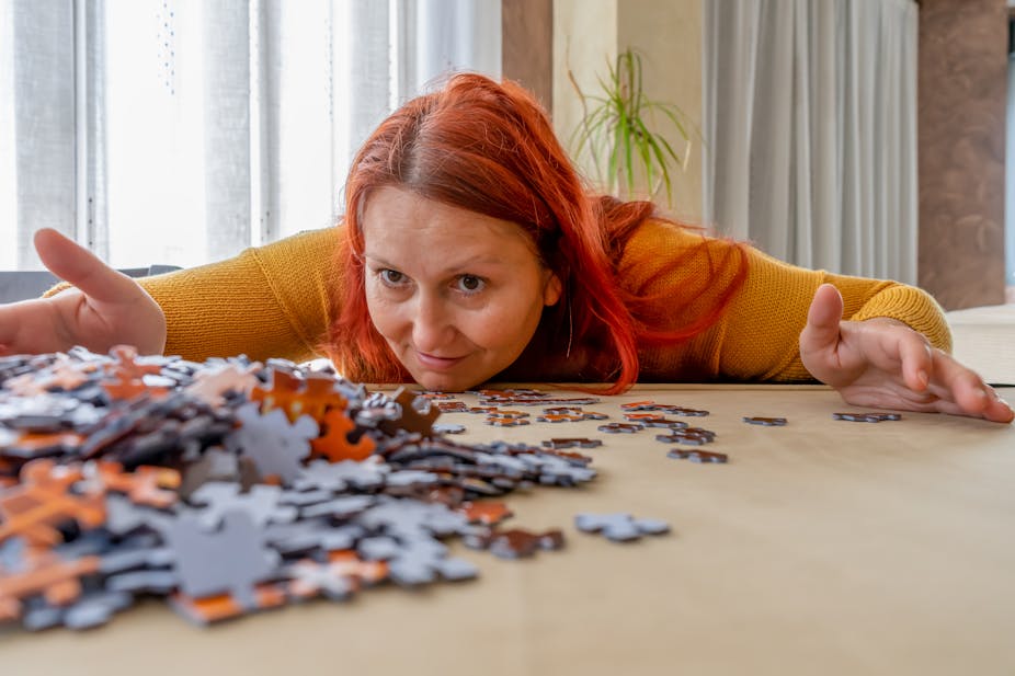 Women bends low over table covered in jigsaw puzzle pieces