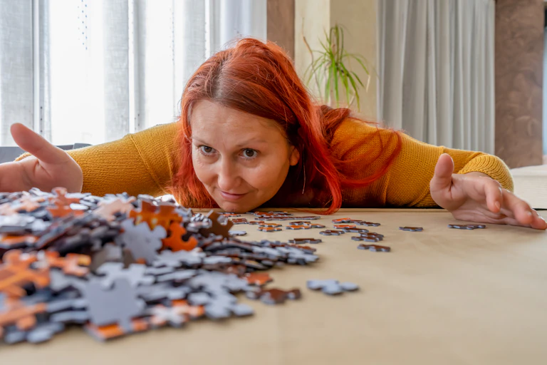 Women bends low over table covered in jigsaw puzzle pieces