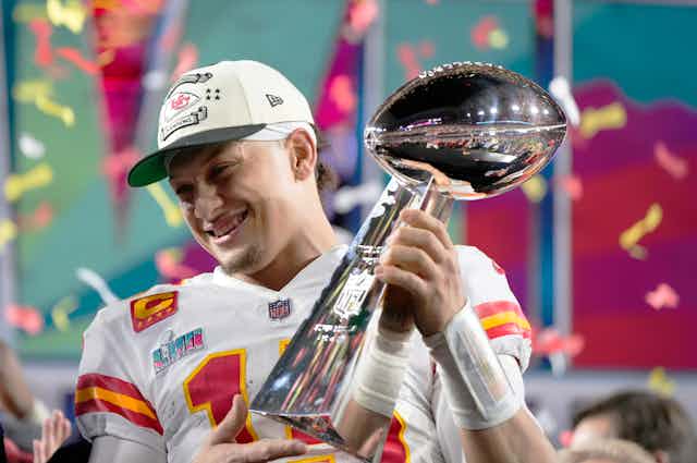 Mahomes smiles as he holds the trophy on the field