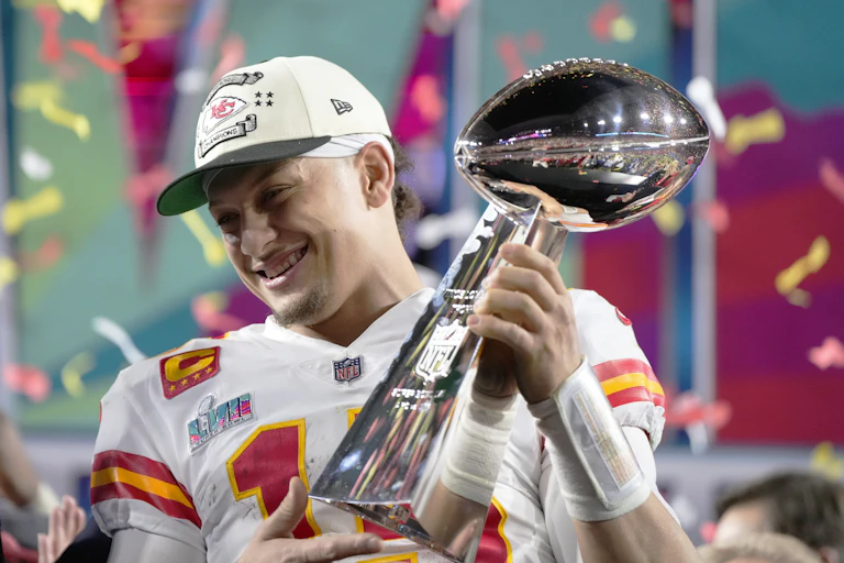 Mahomes smiles as he holds the trophy on the field