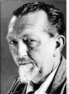 An older man with a white beard looks directly into the camera with a serious expression.