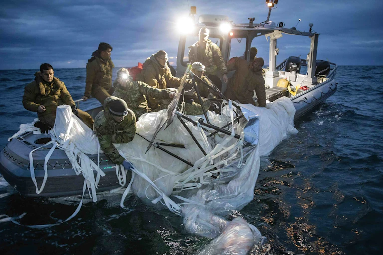 People wearing military gear pull a large piece white fabric out of the water.