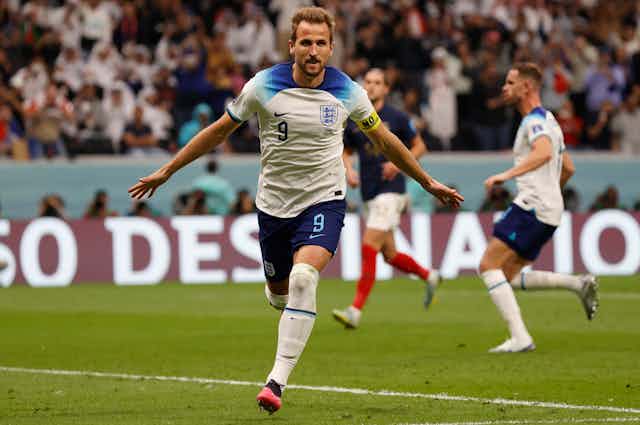 Harry Kane in his England kit. Running with arms out stretched.