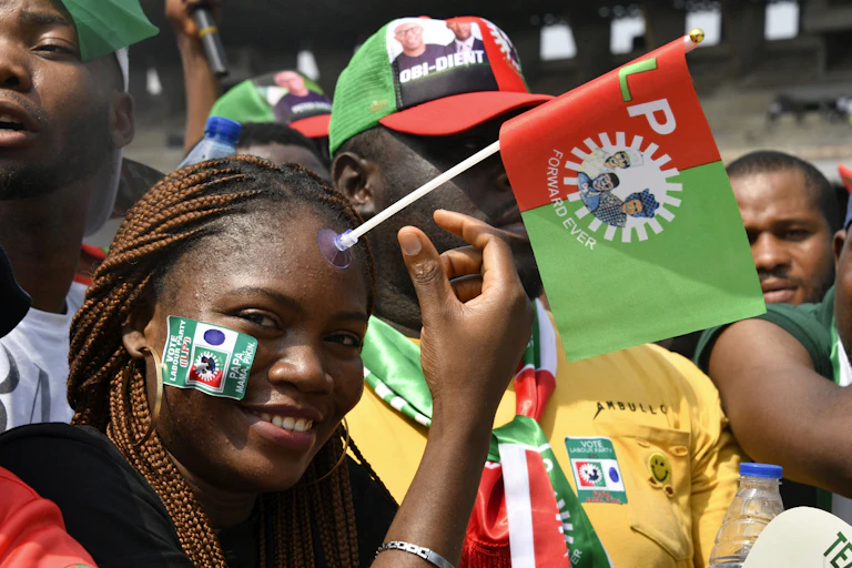 Young smiling woman with election sticker and flag stuck to face stands amid crowd