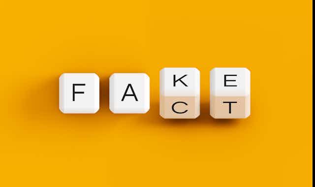 Four cubes with letters on their sides spell out 'Fake' and 'Fact' against an orange backdrop.