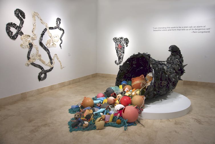 Three large plastic art installations, the central one a cornucopia spilling plastic objects onto the floor.