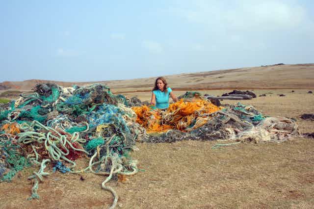 Pam Longobardi sits in a tangle of colored plastic fishing nets on a beach.