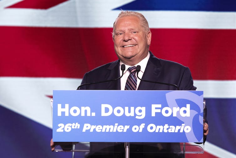 A balding blond man smiles behind a podium that says Hon. Doug Ford.