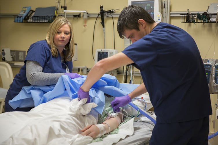 Two health care professionals working on a procedure with a patient lying on a bed.