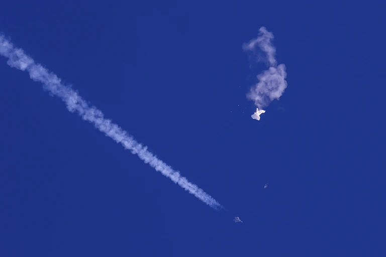 A photo showing wreckage of the Chinese balloon against the background of blue sky, with the vapour trail of a plane.