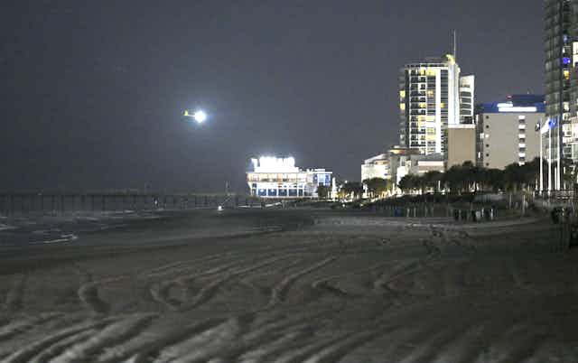 A bright light is seen above a beach with high-rise building in the background.