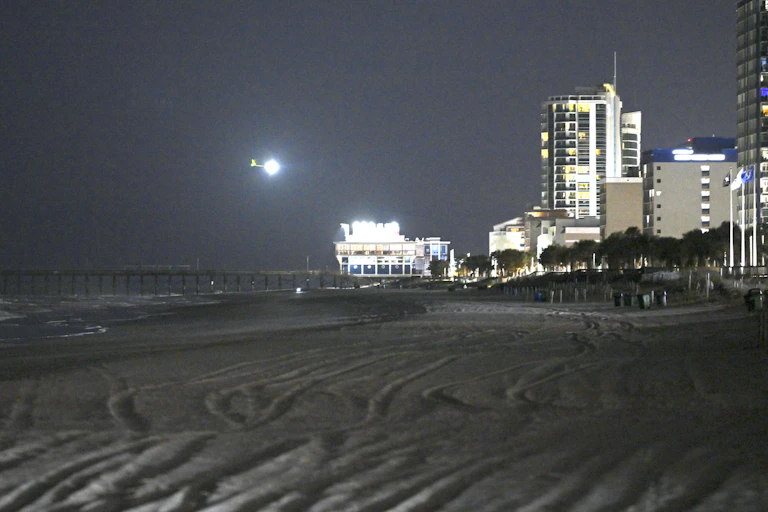 A bright light is seen above a beach with high-rise building in the background.