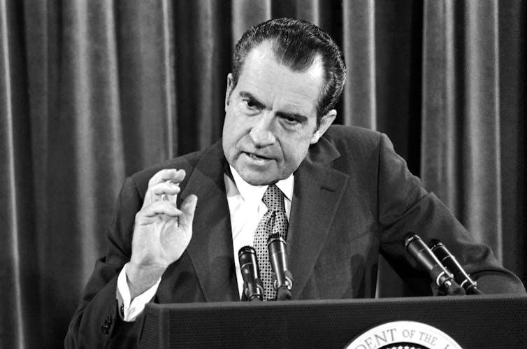 Black and white photo of a man with a receding hairline speaking from behind a podium