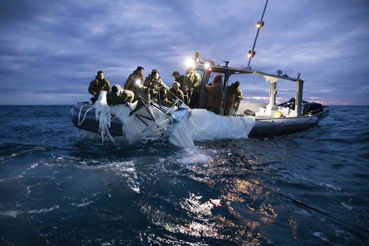 A photo showing people hauling white cloth aboard a boat at sea.