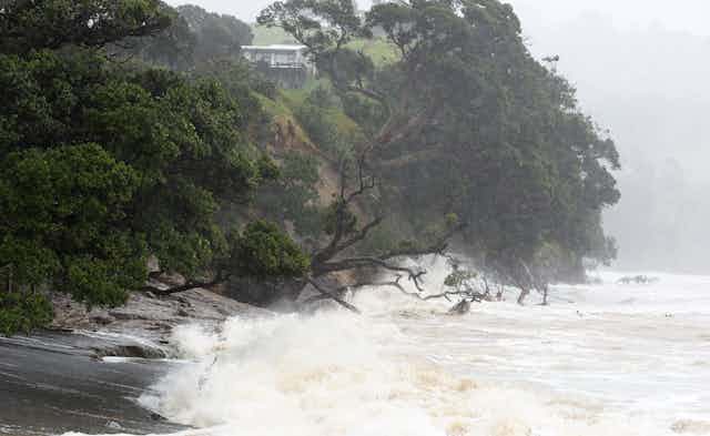 A stretch of coast, with a house on a cliff, pounded by Cyclone Gabrielle