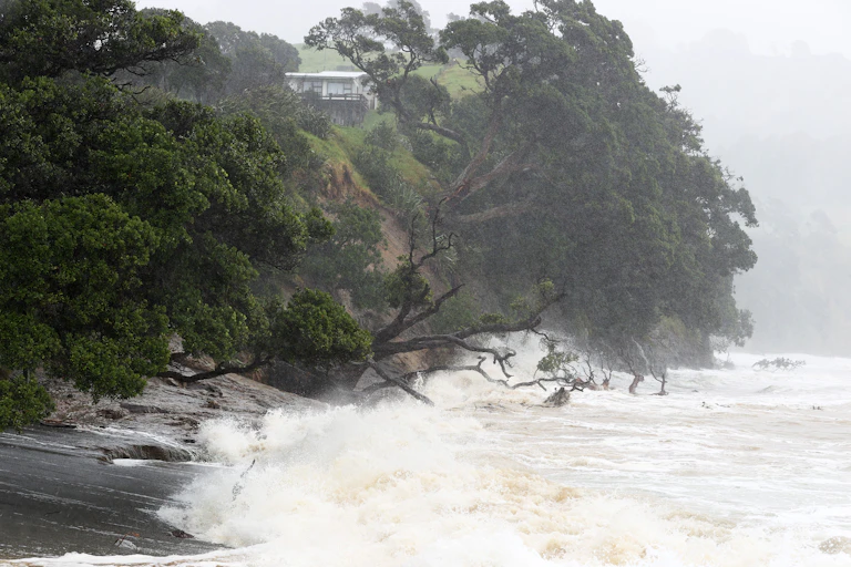 A stretch of coast, with a house on a cliff, pounded by Cyclone Gabrielle